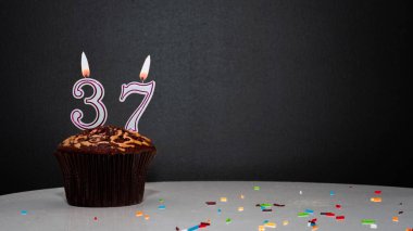 Siyah üzerine muffin, 37 numaralı mumdan bir numara. Kopyalama alanı, siyah arkaplanda bir turta, doğum gününü kutlamak için bir kart, yıldönümü
