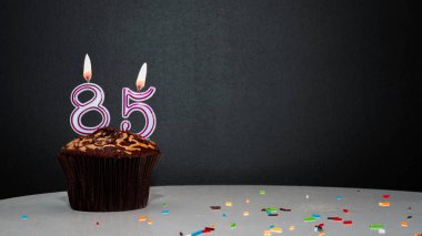 Siyah üzerine kek ve 85 numaralı mumdan bir numara. Kopyalama alanı, siyah arkaplanda bir turta, doğum gününü kutlamak için bir kart, yıldönümü