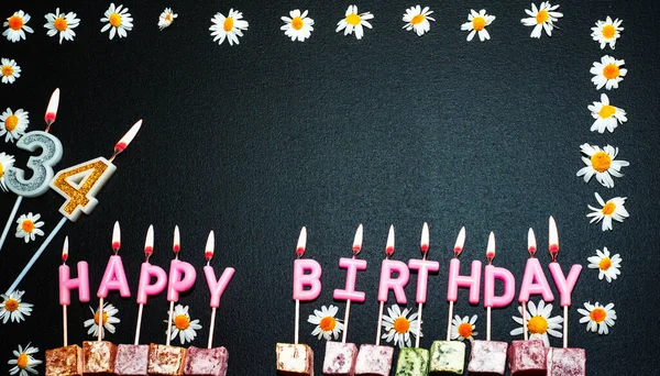 Happy birthday background with number 34. Copy space. Pink happy birthday candles on a black background. Happy birthday flower frame