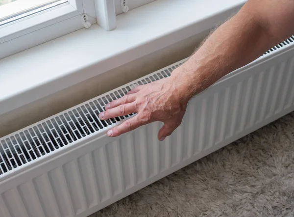 Close-up of a man\'s hands warming themselves by the heating radiator in the apartment. The concept of heating in the room. A person warms himself at home by touching a warm radiator with his hands. The man is frozen at home.