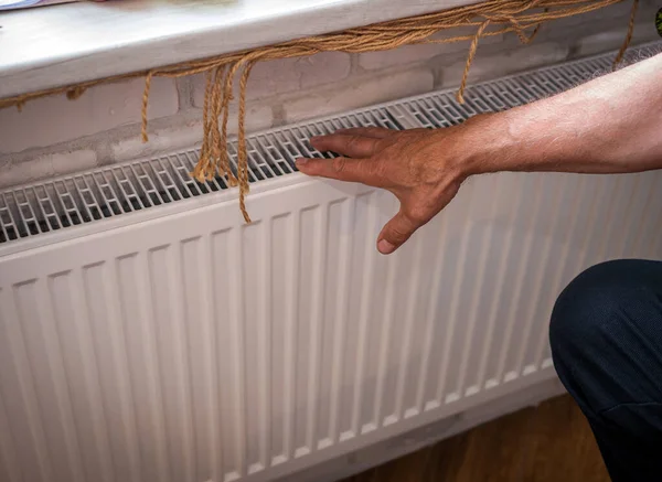 Close-up of a man's hands warming themselves by the heating radiator in the apartment. The concept of heating in the room. A person warms himself at home by touching a warm radiator with his hands. The man is frozen at home.