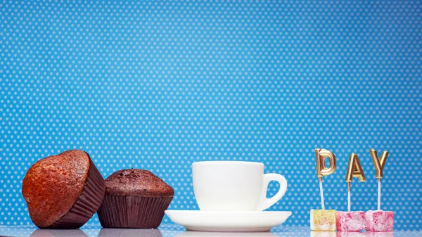 The word day from golden letters with an appetizing muffin and with a cup of coffee on a blue background save space, cupcake fresh close-up. Letters day.
