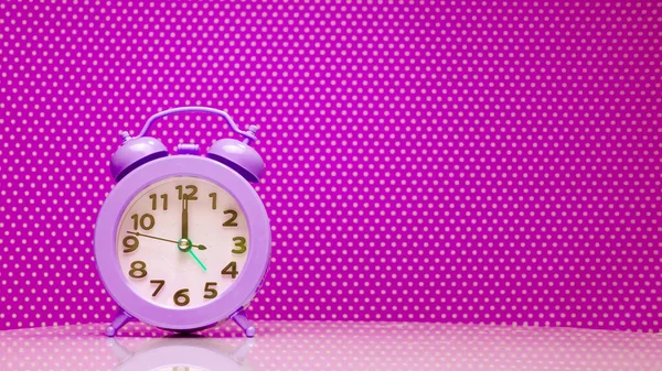 Purple Retro alarm clock on the hands of the clock 12 noon, copy space. Clock display on purple background