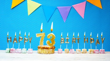 Mavi arkaplandaki 73 numaralı mum harften mutlu yıllar. Beyaz benekli fotokopi alanı. 73 yıllık yanan altın mumlu mutlu yıllar tatlım.