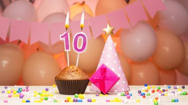 Balonlu süslemeler ve bir çocuk için 10 numaralı doğum günü mumu. Doğum günün kutlu olsun pembe çiçeklerle, on yaşındaki bir kız için fotokopi uzayı. Yanan mumlu kek.