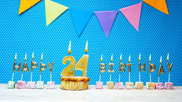 Congratulations on your birthday from the letters of the candles number 24 on a blue background with polka dots white copy space. Happy birthday muffin with burning golden color candle for twenty four
