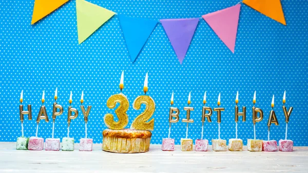 Congratulations on your birthday from the letters of the candles number 32 on a blue background with polka dots white copy space. Happy birthday muffin with burning golden candle for thirty two years old