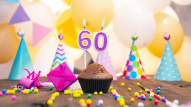 Balonların arka planında altmış yıl boyunca mumlarla mutlu yıllar. Ateşli mumlar ve bir kadın için pembe hediye kutusu olan şenlikli bir kek. Bir kadın için 60 yıl mutlu yıllar..