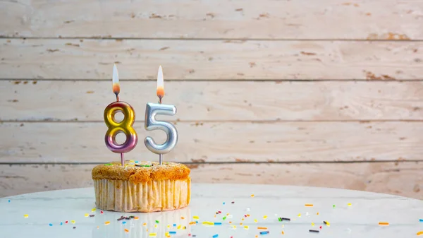 85th birthday greetings from silver numbers on white boards background copy space. Beautiful birthday card with a cupcake with a lit candle for eighty-five years
