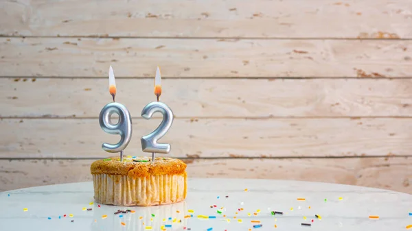 92 year happy birthday greetings from silver numbers on white boards background copy space. Beautiful birthday card with a cupcake with a lit candle for ninety-two years