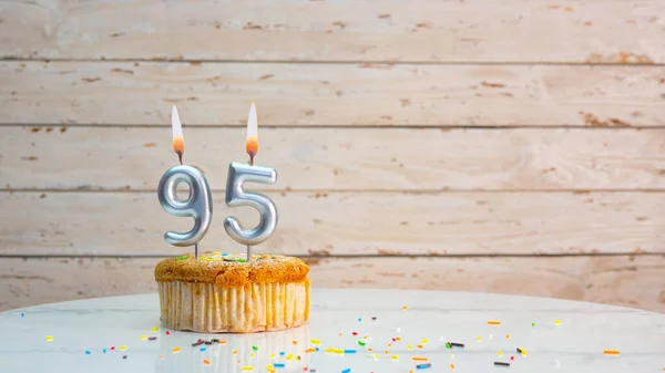 Happy birthday wishes for 95 years from silver numbers on white boards background copy space. Beautiful birthday card with a cupcake with a lit candle for ninety-five years