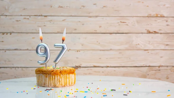 Happy birthday wishes for 97 years from silver numbers on white boards background copy space. Beautiful birthday card with a cupcake with a lit candle for ninety-seven years