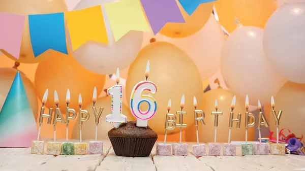 Happy birthday greetings for a child of 16 years old from golden letters of candles burning against the background of mine space balloons. Beautiful birthday card with a muffin for sixteen years