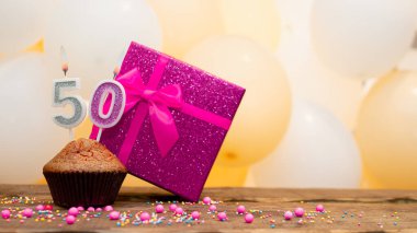 50 yaşındaki kadın için pembe hediye kutusuyla mutlu yıllar. Kek ve 50 numaralı yanan mumla güzel bir doğum günü kartı.