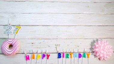 Happy birthday card with number 27. Pink donuts with decorations for a happy birthday from candles.