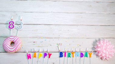 Happy birthday card with number 83. Pink donuts with decorations for a happy birthday from candles