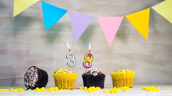 Birthday background with number 38. Beautiful birthday card with colorful garlands, a muffin with a candle burning copyspace