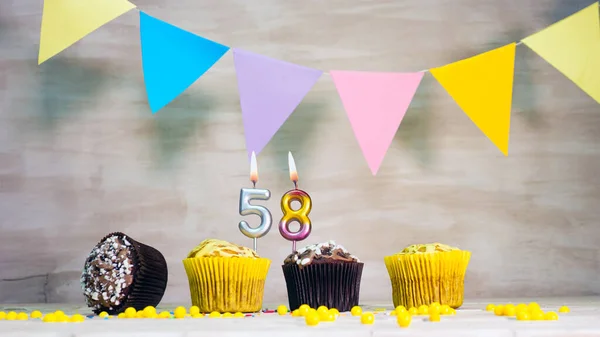 Birthday background with number 58. Beautiful birthday card with colorful garlands, a muffin with a candle burning copyspace