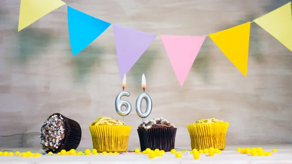 Birthday background with number 60. Beautiful birthday card with colorful garlands, a muffin with a candle burning copyspace