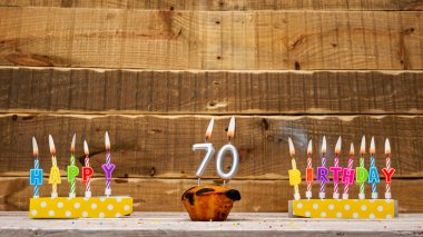 Muffin with a burning candle background for the anniversary on a beautiful wooden background. Postcard with letters of candles with congratulations for the holiday before the birthday. . Copy space. Happy birthday background 70