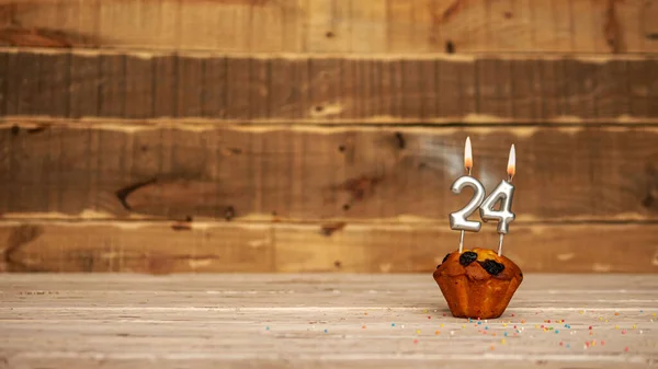 Scenery Festive wooden background happy birthday copy space. Anniversary background with number of burning candles and muffin. Beautiful brown from vintage boards background before a birthday with a number 24