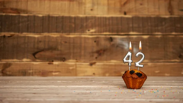 Scenery Festive wooden background happy birthday copy space. Anniversary background with number of burning candles and muffin. Beautiful brown from vintage boards background before a birthday with a number 42