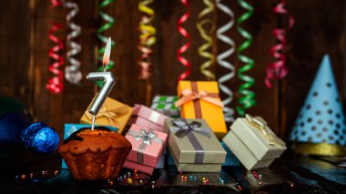 Birthday background with muffin and candles with number  7. Beautiful anniversary background with cake copy space with burning candles. Gift boxes with decorations.