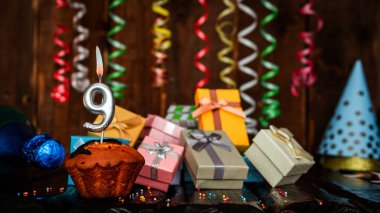 Birthday background with muffin and candles with number  9. Beautiful anniversary background with cake copy space with burning candles. Gift boxes with decorations.