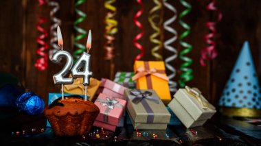 Birthday background with muffin and candles with number  24. Beautiful anniversary background with cake copy space with burning candles. Gift boxes with decorations.