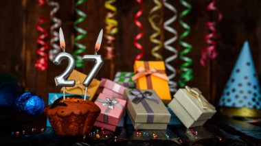 Birthday background with muffin and candles with number  27. Beautiful anniversary background with cake copy space with burning candles. Gift boxes with decorations.