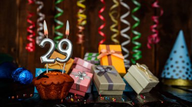 Birthday background with muffin and candles with number  29. Beautiful anniversary background with cake copy space with burning candles. Gift boxes with decorations.