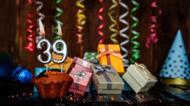 Birthday background with muffin and candles with number  39. Beautiful anniversary background with cake copy space with burning candles. Gift boxes with decorations.