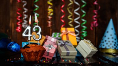 Birthday background with muffin and candles with number  43. Beautiful anniversary background with cake copy space with burning candles. Gift boxes with decorations.