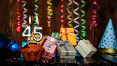 Birthday background with muffin and candles with number  45. Beautiful anniversary background with cake copy space with burning candles. Gift boxes with decorations.