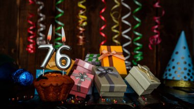 Birthday background with muffin and candles with number  76. Beautiful anniversary background with cake copy space with burning candles. Gift boxes with decorations.