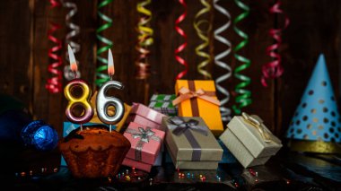 Birthday background with muffin and candles with number  86. Beautiful anniversary background with cake copy space with burning candles. Gift boxes with decorations.