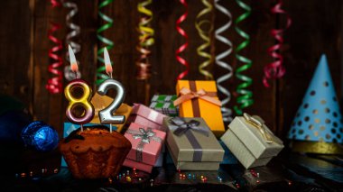 Birthday background with muffin and candles with number  82. Beautiful anniversary background with cake copy space with burning candles. Gift boxes with decorations.