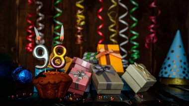 Birthday background with muffin and candles with number  98. Beautiful anniversary background with cake copy space with burning candles. Gift boxes with decorations.