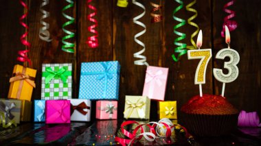 Party birthday background with number  73. Beautiful background anniversary copy space with burning candles. Gift boxes with decorations.