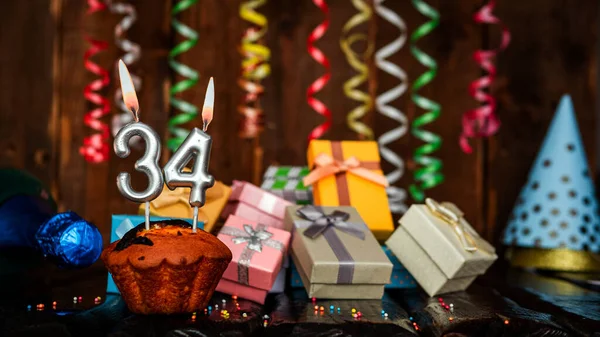 Birthday background with muffin and candles with number  34. Beautiful anniversary background with cake copy space with burning candles. Gift boxes with decorations.