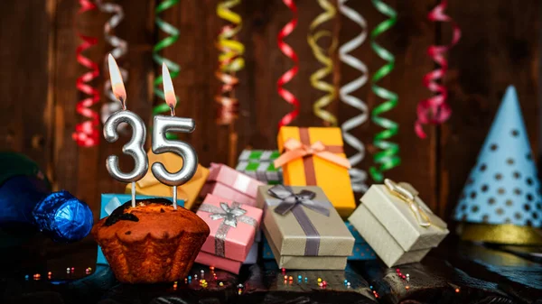 Birthday background with muffin and candles with number  35. Beautiful anniversary background with cake copy space with burning candles. Gift boxes with decorations.