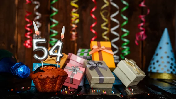 Birthday background with muffin and candles with number  54. Beautiful anniversary background with cake copy space with burning candles. Gift boxes with decorations.