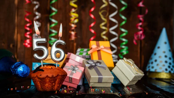 Birthday background with muffin and candles with number  56. Beautiful anniversary background with cake copy space with burning candles. Gift boxes with decorations.