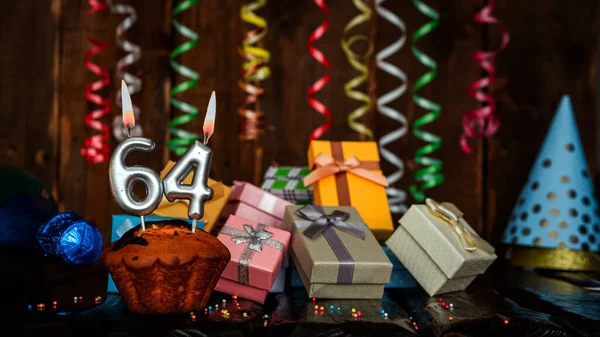 Birthday background with muffin and candles with number  64. Beautiful anniversary background with cake copy space with burning candles. Gift boxes with decorations.
