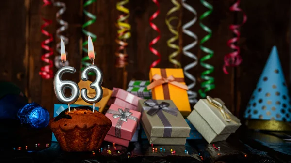 Birthday background with muffin and candles with number  63. Beautiful anniversary background with cake copy space with burning candles. Gift boxes with decorations.