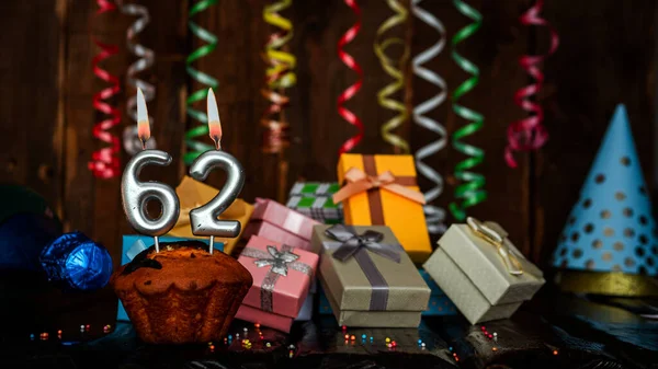 Birthday background with muffin and candles with number  62. Beautiful anniversary background with cake copy space with burning candles. Gift boxes with decorations.