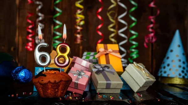 Birthday background with muffin and candles with number  68. Beautiful anniversary background with cake copy space with burning candles. Gift boxes with decorations.