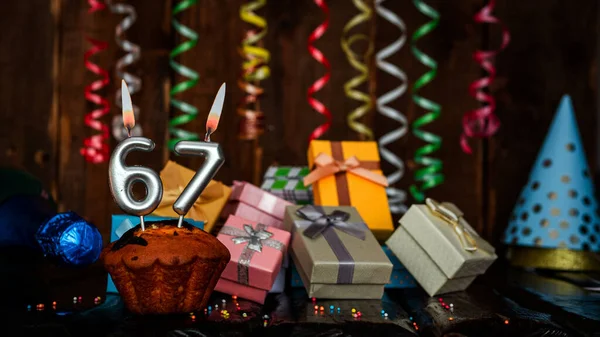 Birthday background with muffin and candles with number  67. Beautiful anniversary background with cake copy space with burning candles. Gift boxes with decorations.