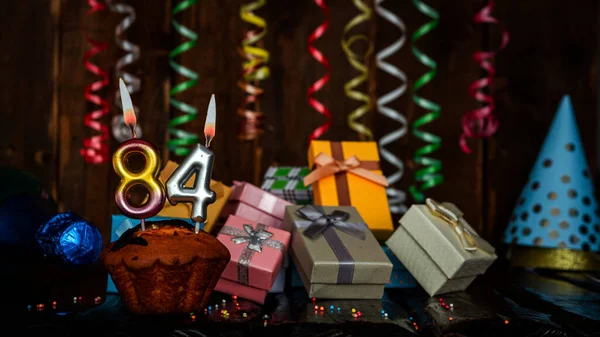 Birthday background with muffin and candles with number  84. Beautiful anniversary background with cake copy space with burning candles. Gift boxes with decorations.