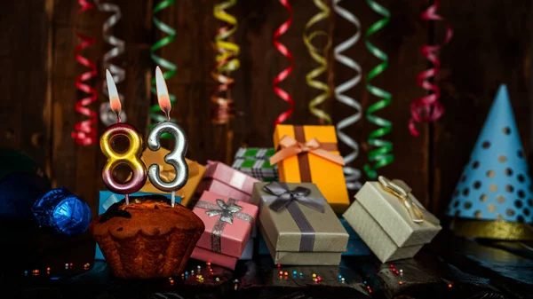 Birthday background with muffin and candles with number  83. Beautiful anniversary background with cake copy space with burning candles. Gift boxes with decorations.